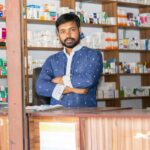 A confident pharmacist stands behind the counter of a pharmacy in Natore, Bangladesh.